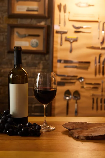 Close-up de garrafa de vinho tinto com vidro e uvas na mesa de madeira — Fotografia de Stock