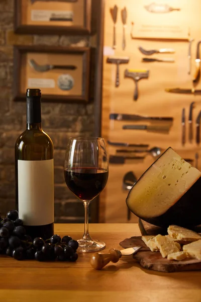 Primo piano di formaggio di delicatezza affettato con vino rosso e uva su tavola rustica — Foto stock