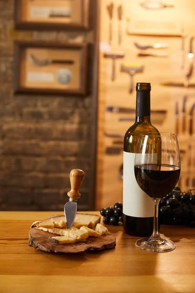 Primer plano de queso en rodajas con vino tinto y uvas sobre mesa rústica - foto de stock
