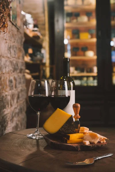 Fette di formaggio e bicchieri di vino rosso su tavolo di legno rustico — Foto stock
