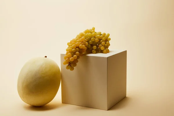 Primer plano de melón maduro y uvas con cubo en superficie beige - foto de stock