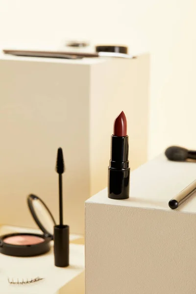 Close-up shot of red lipstick with various makeup accessories on beige cubes — Stock Photo