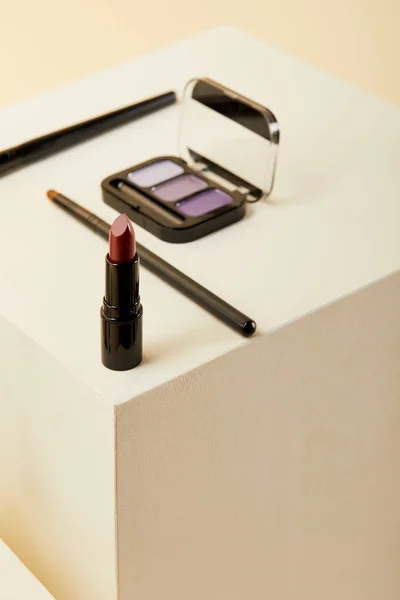 Close-up shot of lipstick with purple eyeshadows case and brushes on beige — Stock Photo