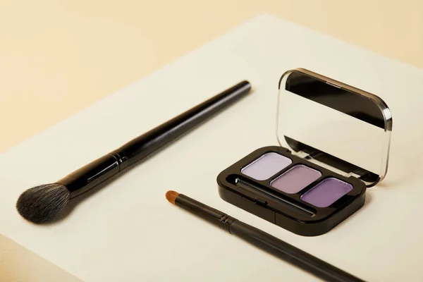 Close-up shot of purple eyeshadows case with brushes on beige — Stock Photo