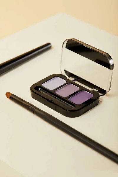 Close-up shot of purple eyeshadows case with brush on beige — Stock Photo