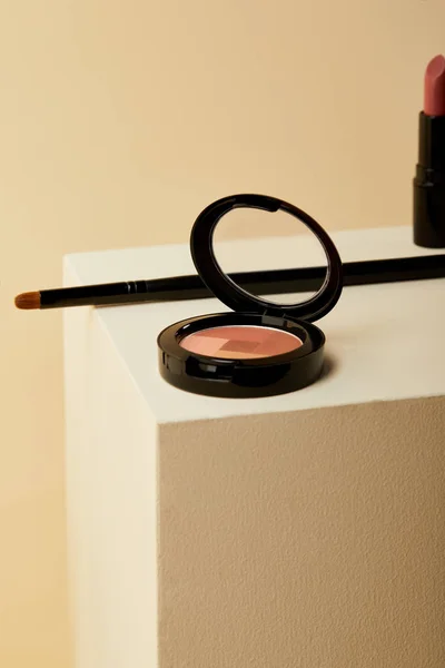 Close-up shot of blush can with lipstick and applicator on beige cube — Stock Photo