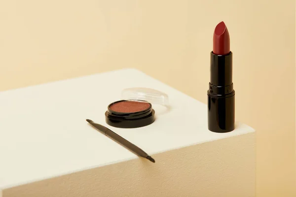 Gros plan de rouge à lèvres debout sur la surface beige avec boîte de blush et brosse — Photo de stock