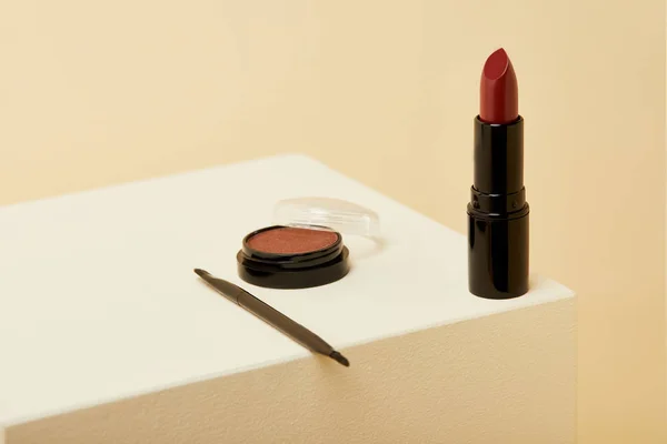 Primer plano de lápiz labial de pie en la superficie beige con lata de rubor y cepillo - foto de stock