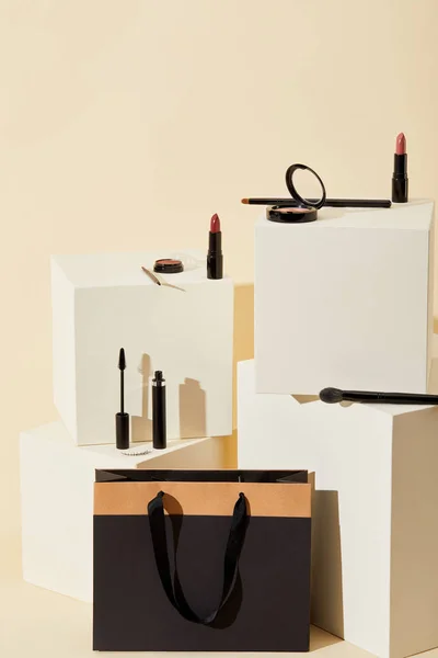 Various makeup supplies lying on beige cubes with paper bag — Stock Photo