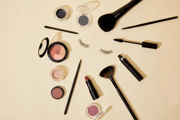Top view of different cosmetics lying on beige surface around false eyelashes — Stock Photo