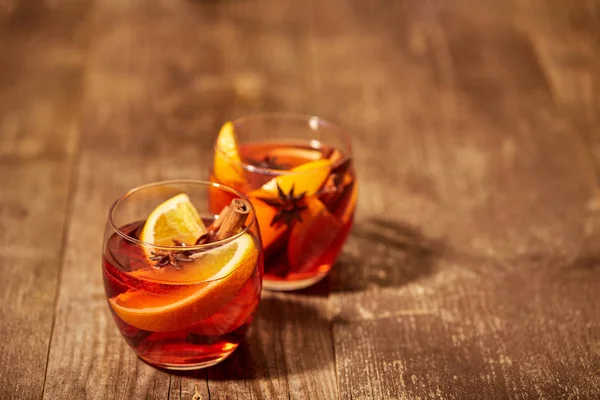 Close up view of hot mulled wine drinks with spices and orange pieces on wooden tabletop — Stock Photo