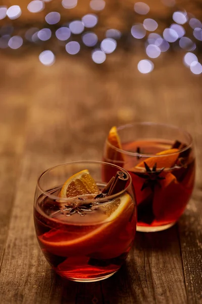 Close up view of delicious hot mulled wine in glasses with orange pieces on wooden tabletop with bokeh lights on backdrop — Stock Photo