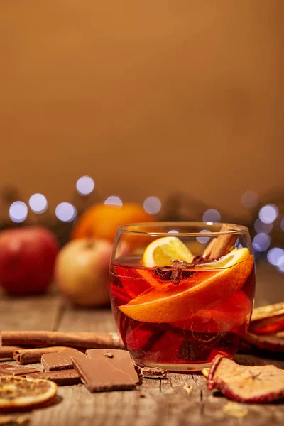 Close up view of mulled wine drink, chocolate and spices on wooden surface with bokeh lights on background — Stock Photo