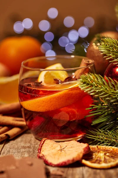 Vue rapprochée de la boisson au vin chaud avec des morceaux d'orange et des épices sur la surface en bois avec des lumières bokeh sur fond — Photo de stock