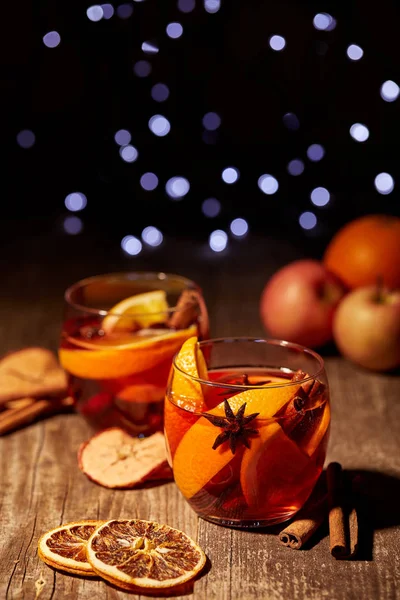 Vista de cerca de deliciosas bebidas de vino caliente caliente con especias en la mesa de madera con luces bokeh desenfocadas en el fondo - foto de stock