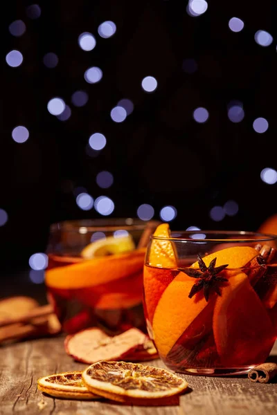 Vista de perto de deliciosas bebidas quentes de vinho quente e especiarias em mesa de madeira com luzes de bokeh desfocadas no fundo — Fotografia de Stock