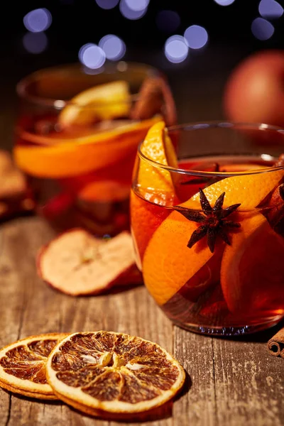 Vista da vicino di deliziose bevande calde al vin brulè e spezie su un tavolo in legno con luci soffuse bokeh sullo sfondo — Foto stock