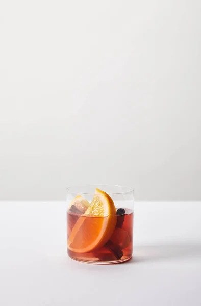 Close up view of hot mulled wine in glass with orange pieces on white tabletop on grey background — Stock Photo