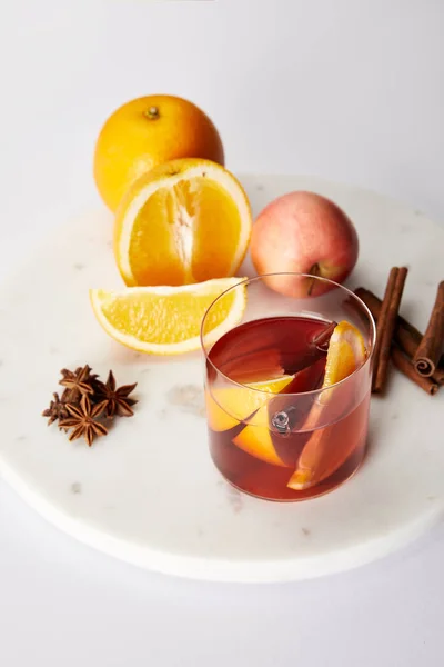 Close up view of hot mulled wine in glass, spices, oranges and apple on white tabletop — Stock Photo