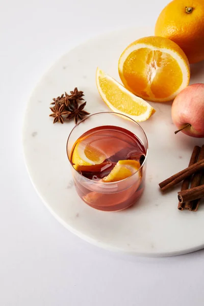 Vista de perto do vinho quente mulled em vidro, especiarias e frutas frescas na superfície branca — Fotografia de Stock