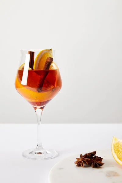 Vue rapprochée du vin chaud savoureux avec des morceaux d'orange et des étoiles d'anis sur la table blanche sur fond gris — Photo de stock