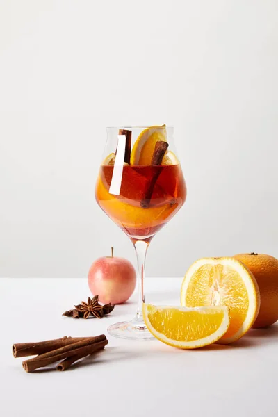 Vue rapprochée du vin chaud en verre et des ingrédients disposés sur une table blanche sur fond gris — Photo de stock