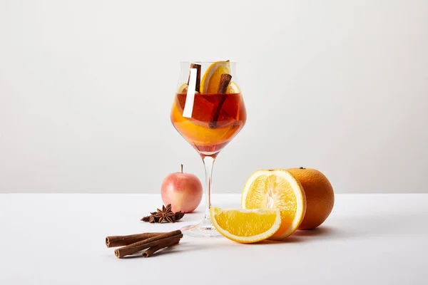 Nahaufnahme von Glühwein im Glas und herumliegenden Zutaten auf weißer Tischplatte vor grauem Hintergrund — Stockfoto