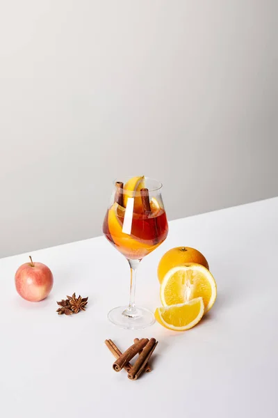 Vue rapprochée du vin chaud en verre et des ingrédients disposés sur une table blanche sur fond gris — Photo de stock