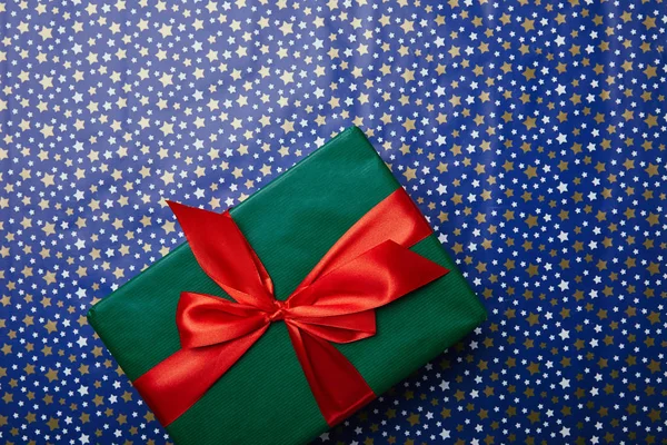 Top view of green gift with red ribbon on festive wrapping paper with stars pattern — Stock Photo