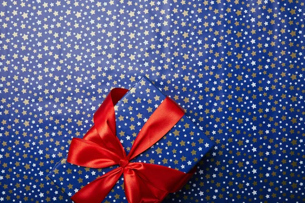 Vista superior de la caja de regalo envuelta con cinta roja en papel de regalo festivo con patrón de estrellas - foto de stock