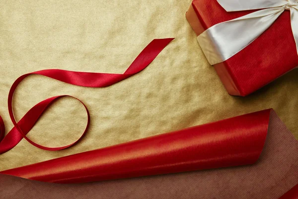 Vista superior del regalo y la cinta en el fondo de papel de regalo rojo y dorado - foto de stock