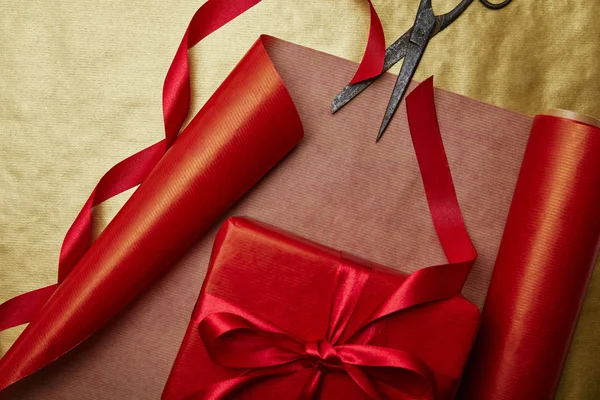 Top view of scissors and christmas present with ribbon on red and golden wrapping papers background — Stock Photo