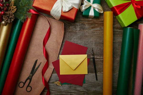 Flat lay with different wrapping papers, chrtismas toys on pine tree branch, wrapped presents and blank envelopes on wooden tabletop — Stock Photo