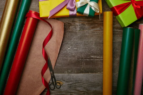 Ansicht des Arrangements von Geschenkpapieren, Weihnachtsgeschenken mit Schleifen und Scheren auf Holztischplatte — Stockfoto