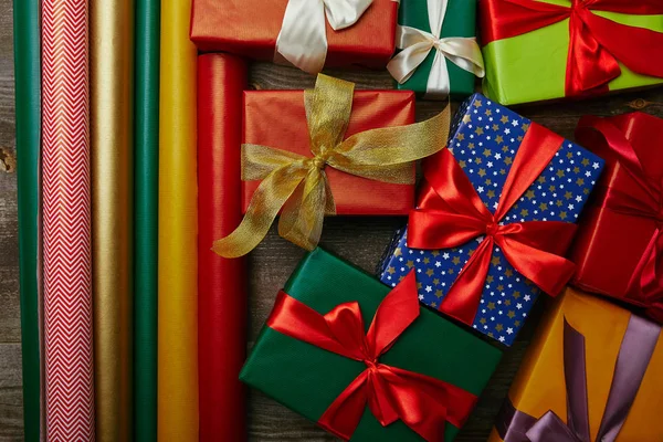 Top view of arrangement of various wrapping papers and new year presents with ribbons on wooden tabletop — Stock Photo