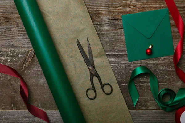 Posa piatta con busta bianca, forbici, carta da regalo e nastri per regali di Natale su tavolo in legno — Foto stock