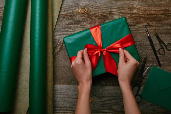 Cropped shot of woman tying ribbon on present on wooden tabletop with wrapping paper — Stock Photo