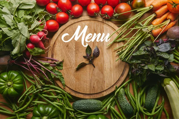 Variedad de verduras y hierbas frescas por tabla de cortar con letras de 