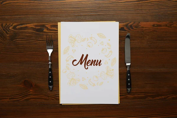 Vista superior del menú con tenedor y cuchillo en mesa de madera - foto de stock