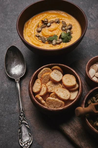 Tazón con sopa de calabaza, cuchara y rusks en la superficie oscura - foto de stock