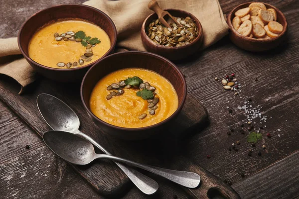 Gustosa zuppa di zucca sana con semi in ciotole e cucchiai su tavolo di legno — Foto stock
