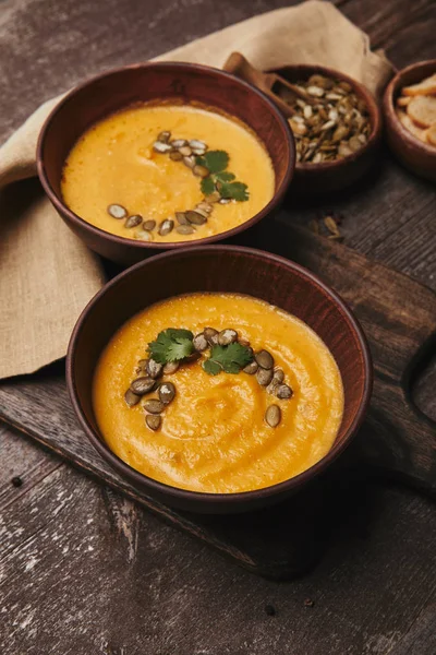 Vista ravvicinata di deliziosa zuppa di zucca con semi in ciotole su tavolo di legno — Foto stock