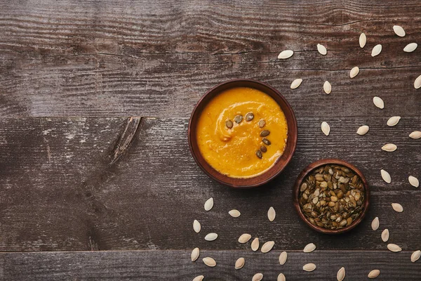 Vue du dessus des bols avec une délicieuse soupe à la citrouille et des graines sur une table en bois rustique — Photo de stock