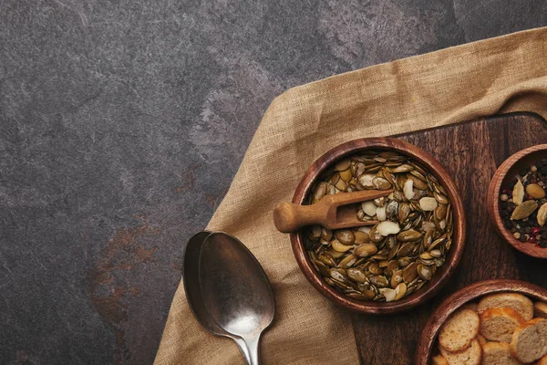 Vista dall'alto di ciotola con semi di zucca, cucchiai, spezie e fette biscottate su sacco — Foto stock