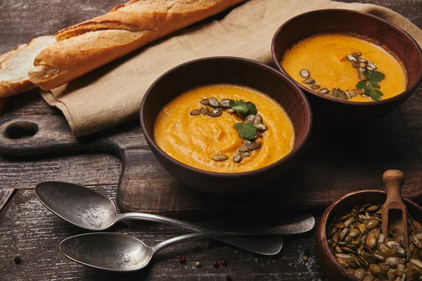Close-up view of bowls with pumpkin soup, spoons and pumpkin seeds on wooden table — Stock Photo