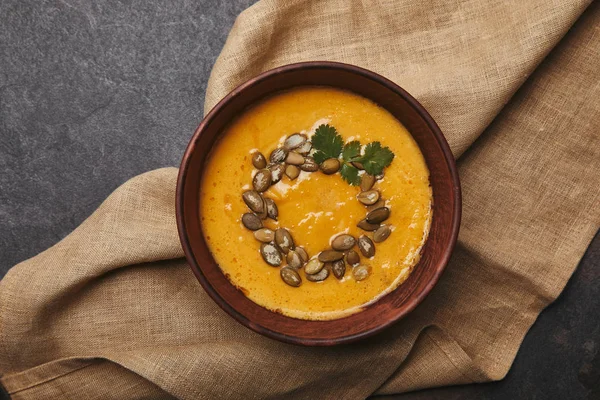 Vista dall'alto di gustosa zuppa di zucca sana con semi in ciotola su sacco — Foto stock