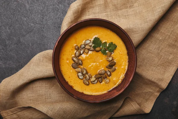 Vue du dessus de soupe de citrouille savoureuse et saine avec des graines dans un bol sur un sac — Photo de stock