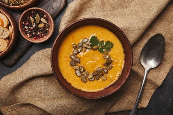 Top view of bowl with delicious pumpkin soup and spoon on sackcloth — Stock Photo