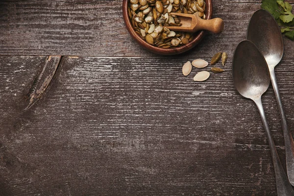 Vista dall'alto di ciotola con semi di zucca e cucchiai su tavolo rustico in legno — Foto stock