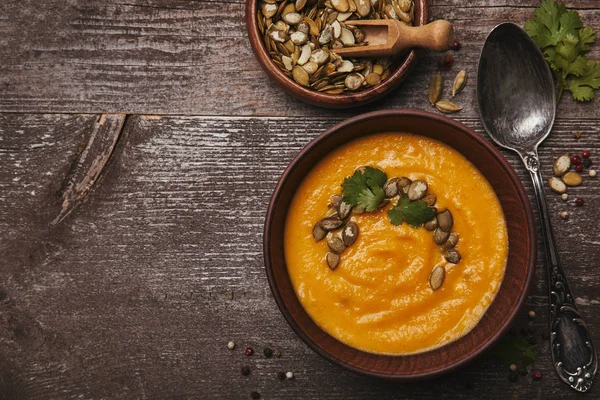 Top view of bowl with delicious pumpkin soup, spoon and pumpkin seeds on wooden table — Stock Photo